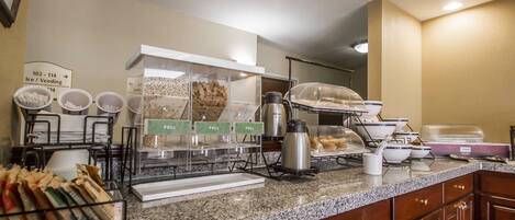 A breakfast buffet area with labeled containers for food items, a coffee station, and a sign indicating the location of ice and vending machines.