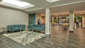 A spacious lobby with a high ceiling, a skylight, a seating area with two sofas, a patterned rug, and a dining area with tables and chairs. - Wingate by Wyndham Biloxi/Ocean Springs (Biloxi)