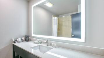 A modern bathroom with a large mirror, a sink, and a shower visible in the reflection.