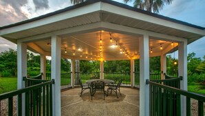 A covered outdoor patio with a table and chairs, string lights, and a view of greenery. - Wingate by Wyndham Biloxi/Ocean Springs (Biloxi)