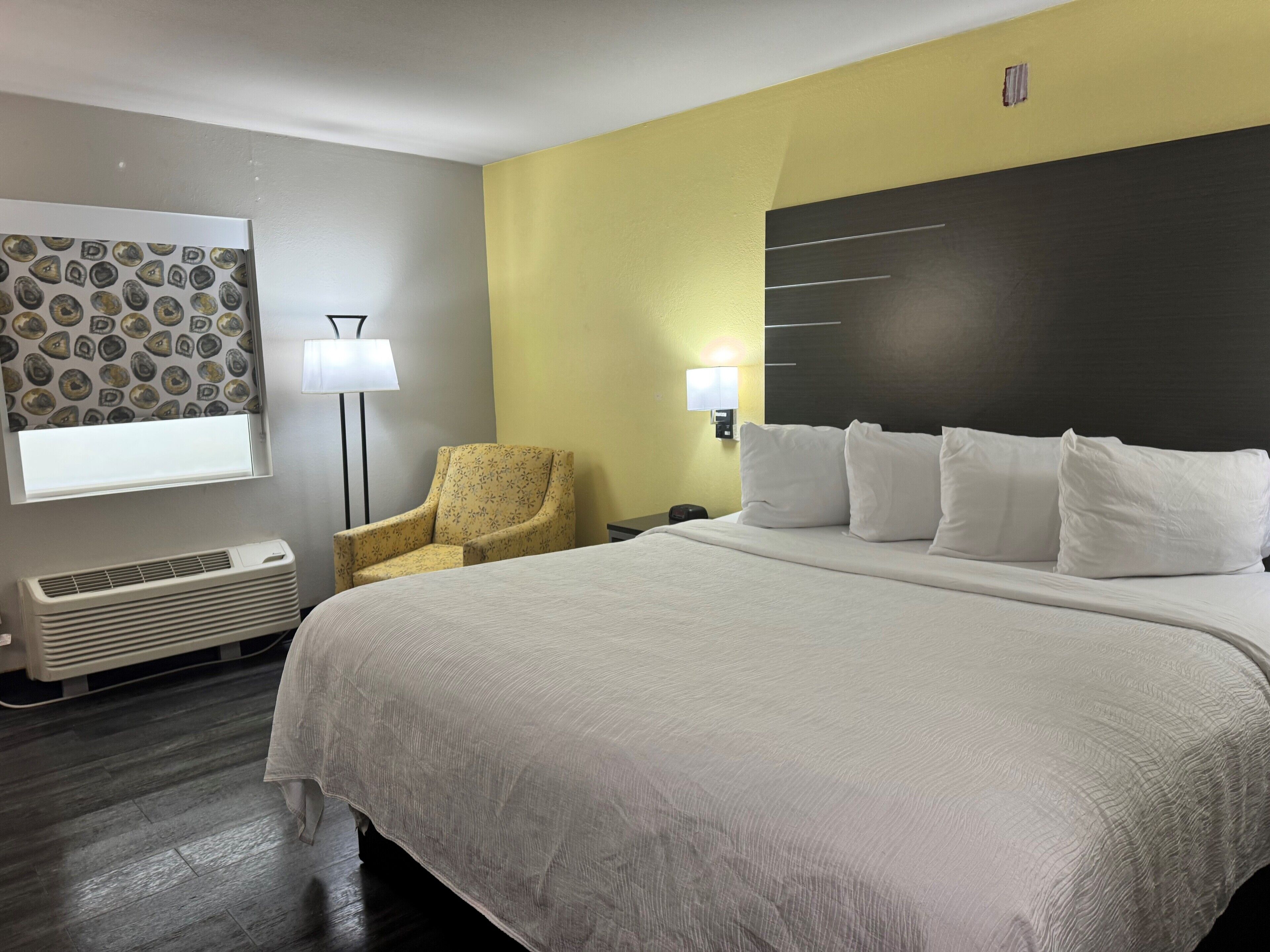 A hotel room with a large bed, a chair, a lamp, and a wall with a patterned design.