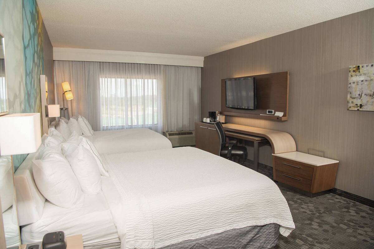 A hotel room with a large bed, a desk with a chair, a flat-screen TV, and a small cabinet.