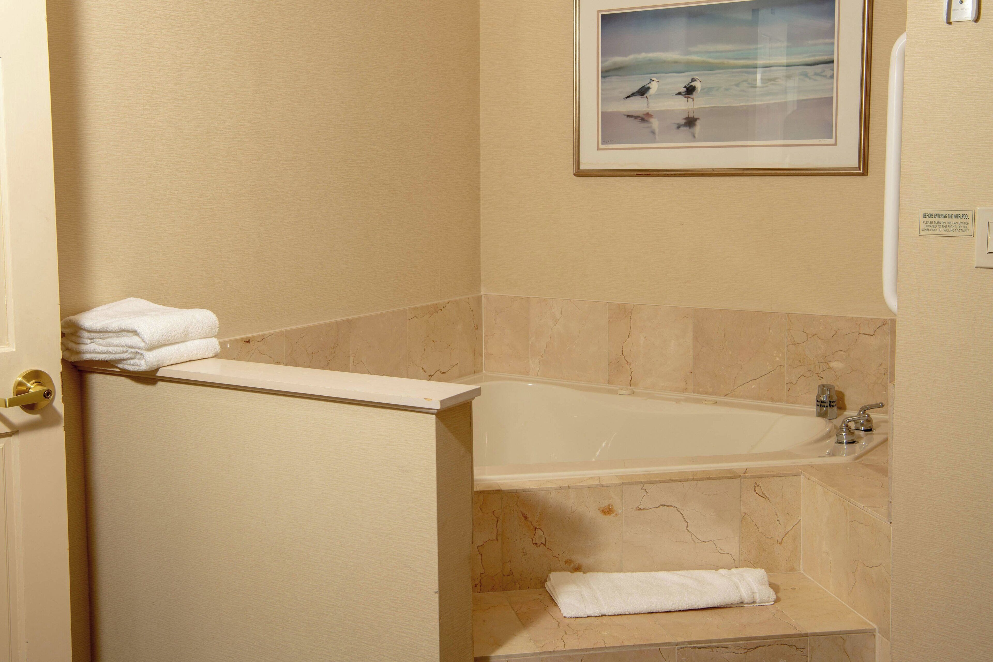 A bathroom with a bathtub, marble walls, and a framed picture of birds on the wall.