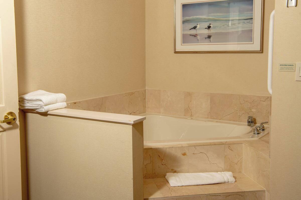 A bathroom with a bathtub, marble walls, and a framed picture of birds on the wall.