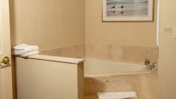 A bathroom with a bathtub, marble walls, and a framed picture of birds on the wall.