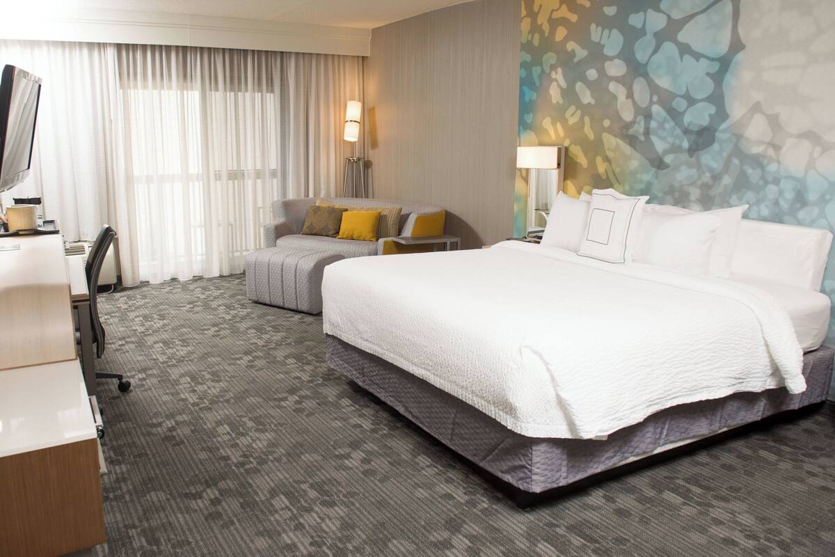 A hotel room with a large bed, a desk, a chair, and a television.