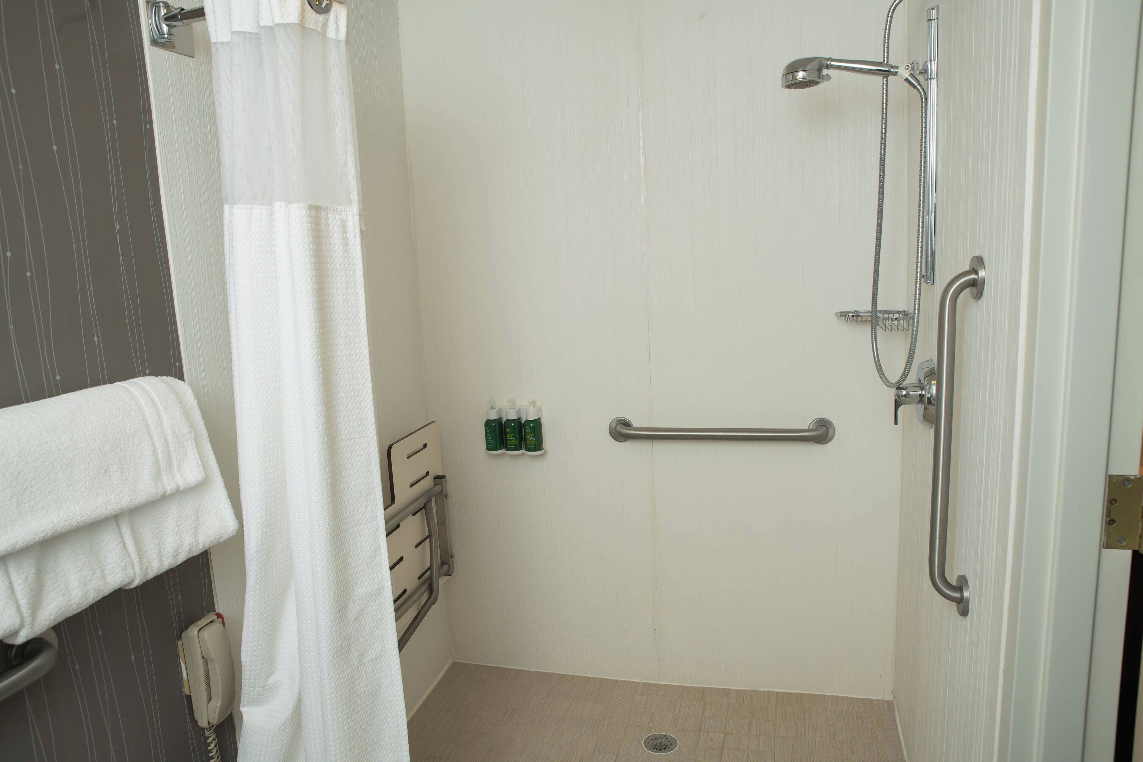 A bathroom with a shower, grab bars, a towel rack, and a hand dryer.