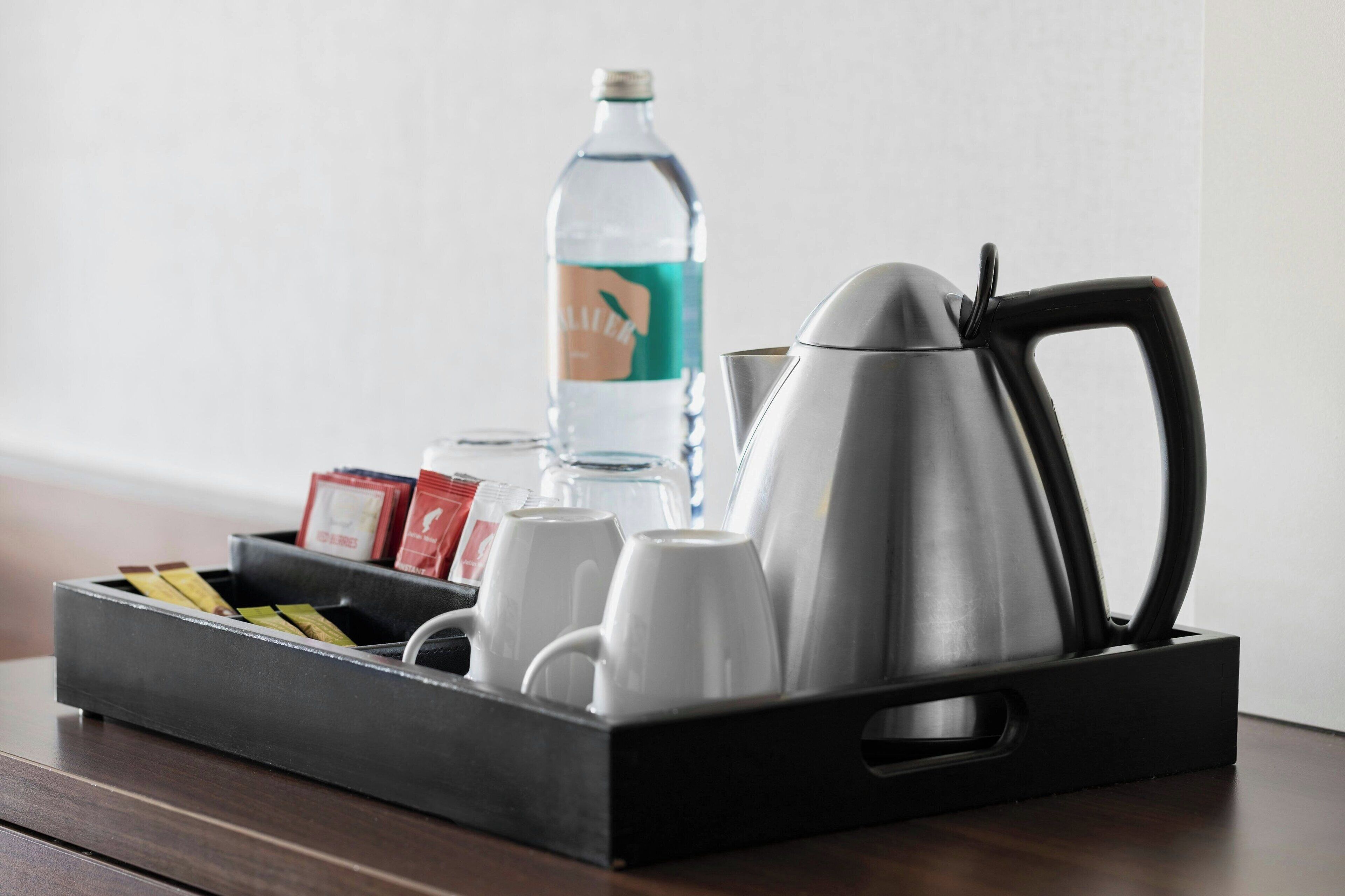 Una bandeja con una tetera, tazas, una botella de agua y algunos aperitivos envasados sobre una mesa de madera.
