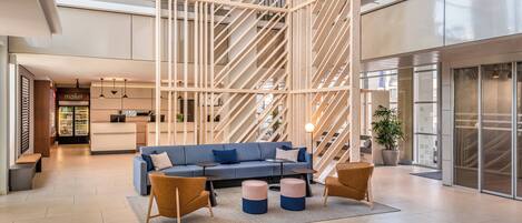A spacious lobby with a blue sofa, two ottomans, and a staircase.