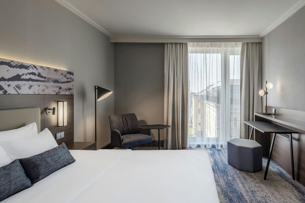 Una habitación de hotel con una cama grande, un escritorio, una silla y vistas a la ciudad por la ventana.