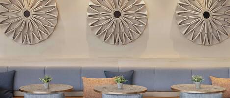 A modern interior with three round tables, each with a plant, set against a beige wall with three large, circular wall art pieces.