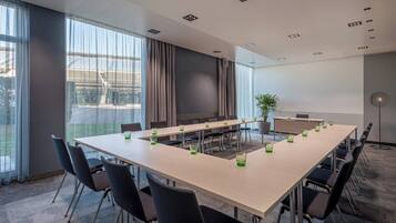 Un salón de conferencias con una larga mesa, sillas y una pantalla de proyector.