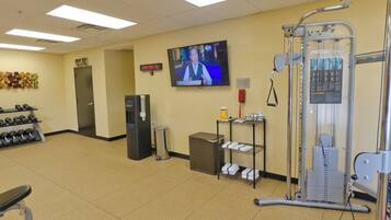 A gym with exercise equipment, a television, and a wall clock.