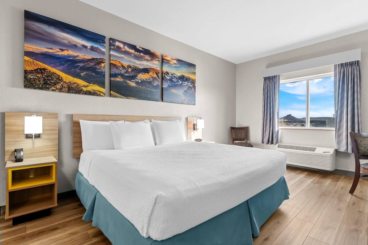 Habitación de hotel con una cama grande, dos lámparas de pared, una mesita de noche, una silla y una ventana con cortinas.