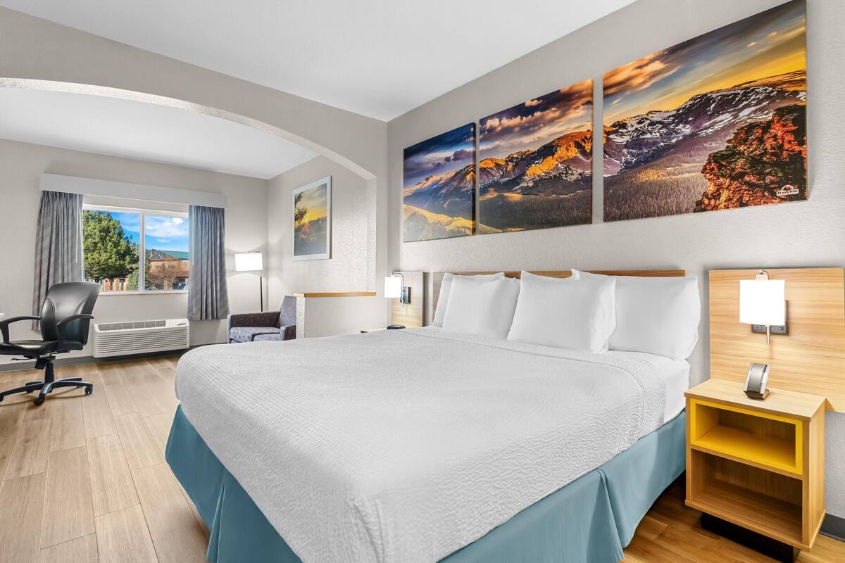 Una habitación de hotel con una cama grande, un escritorio, una silla y una ventana con cortinas.