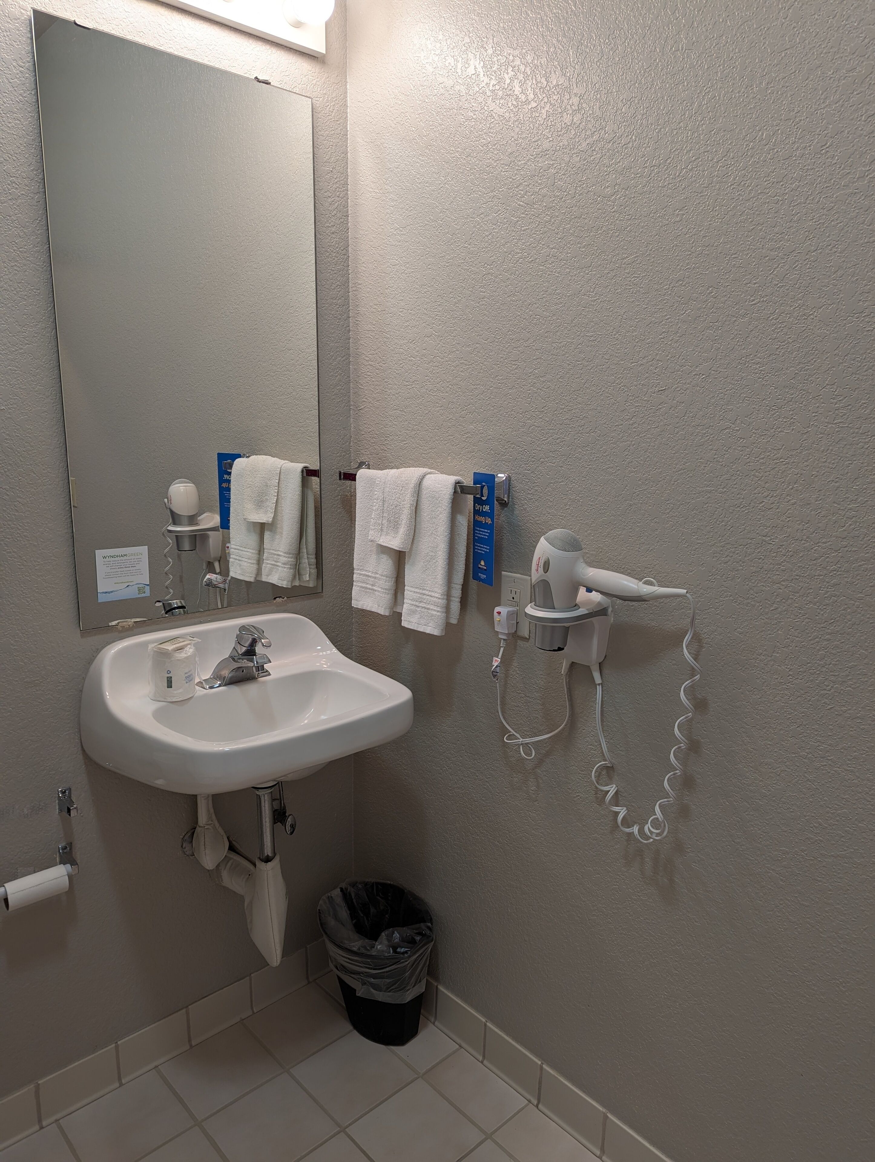 Un baño con lavamanos, espejo, toallero y secador de pelo.