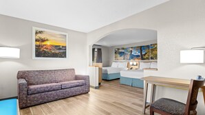 Une chambre d’hôtel moderne, équipée d’un canapé, d’un bureau et d’une chaise. Les murs sont ornés de tableaux et une fenêtre est agrémentée de rideaux.