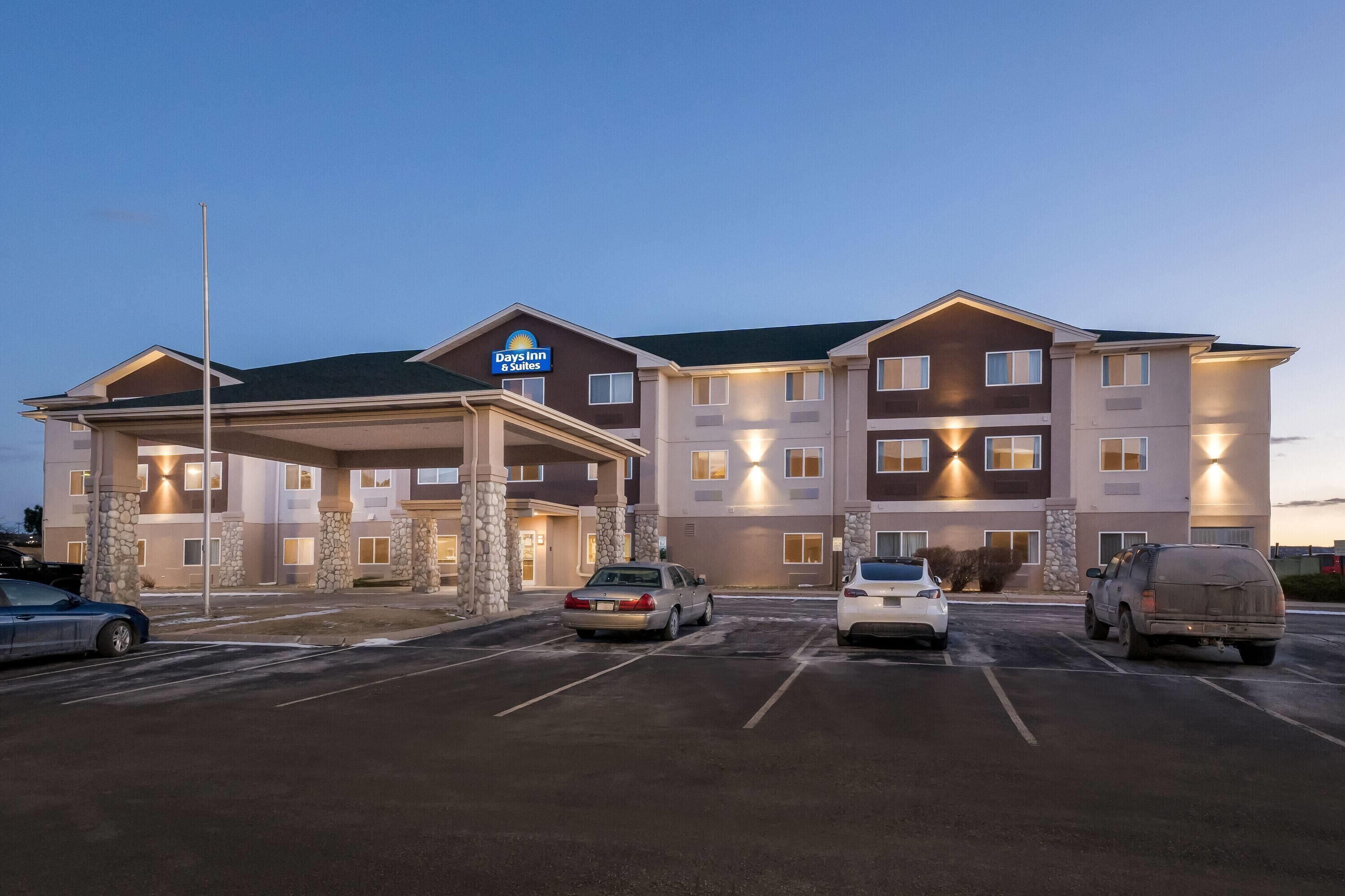 Edificio de Days Inn & Suites con entrada cubierta, varios pisos y un estacionamiento con varios automóviles.