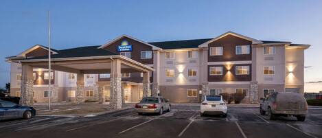 Edificio de Days Inn & Suites con entrada cubierta, varios pisos y un estacionamiento con varios automóviles.