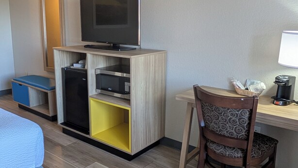 A hotel room with a bed, a desk with a chair, a television, a microwave, and a coffee maker. - Days Inn & Suites by Wyndham Castle Rock (Castle Rock)
