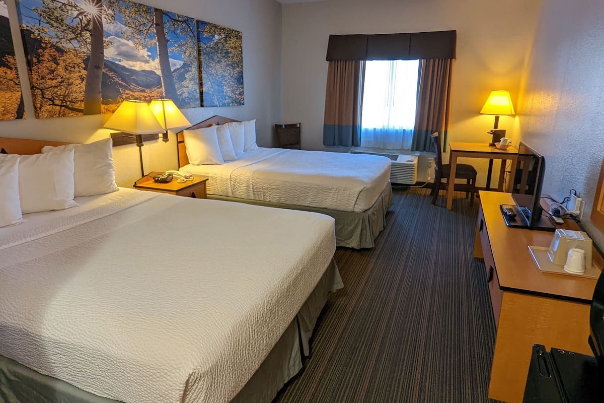 Una habitación de hotel con dos camas, un escritorio, una silla, una lámpara y un cuadro en la pared.
