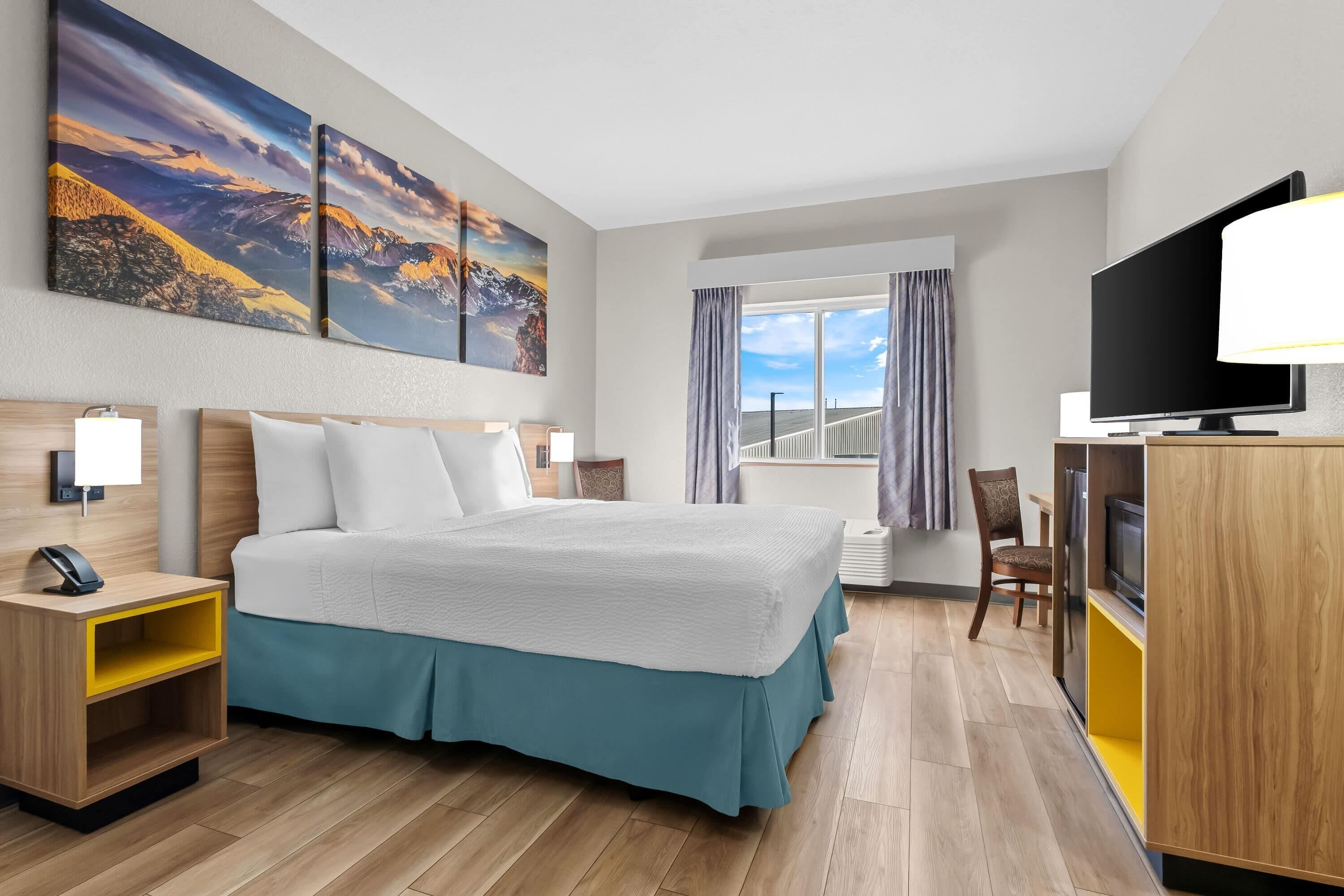 Une chambre d’hôtel avec un grand lit, une télévision, un bureau avec une chaise et des œuvres d’art accrochées au mur.