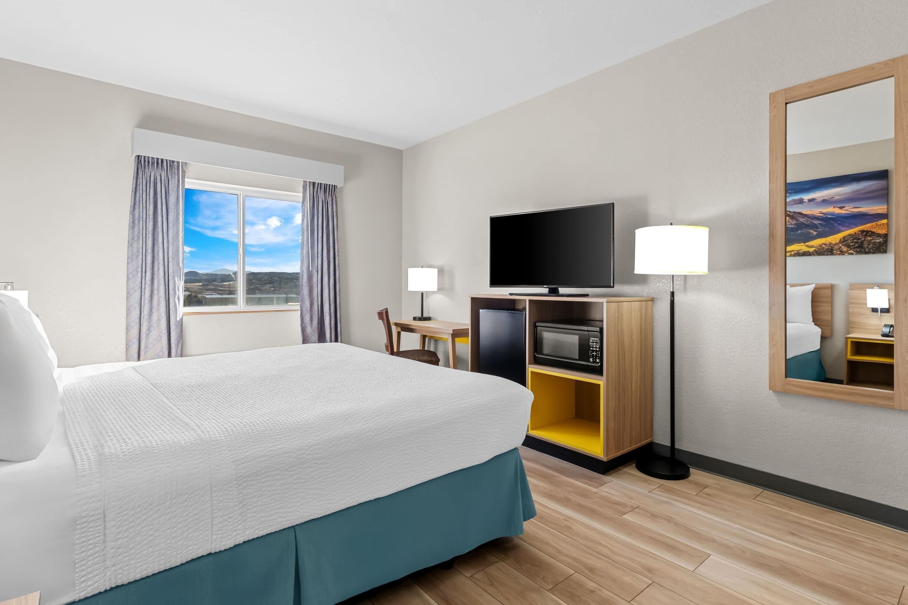 Hotelkamer met een groot bed, een televisie, een bureau met stoel, een lamp, een magnetron en uitzicht op het omliggende landschap.