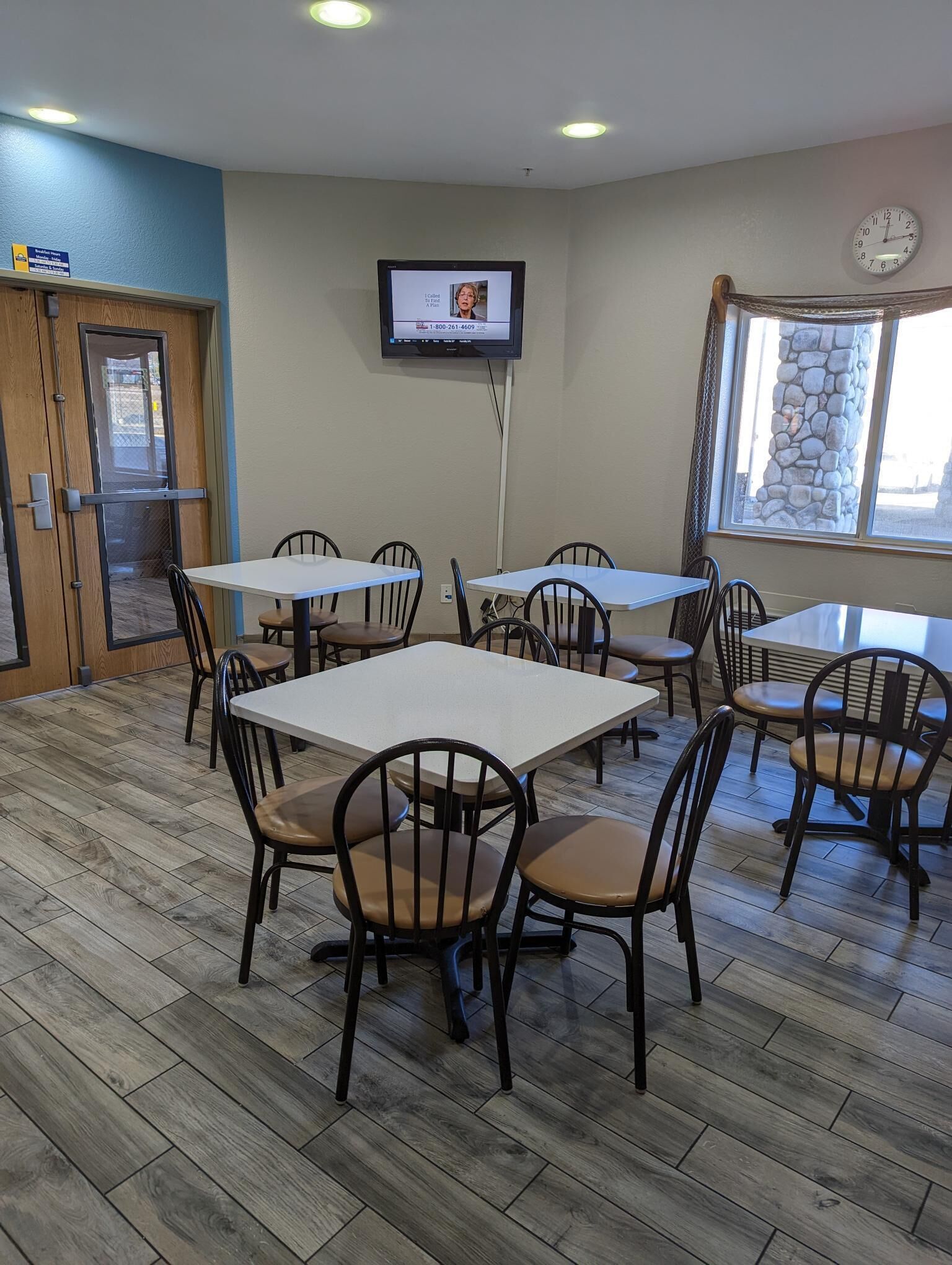 A dining area with multiple tables and chairs, a television mounted on the wall, and a clock on the wall.