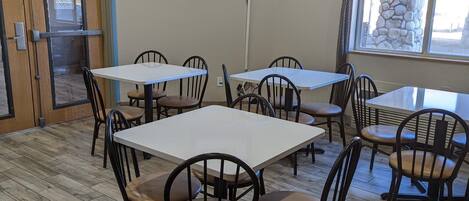 A dining area with multiple tables and chairs, a television mounted on the wall, and a clock on the wall.