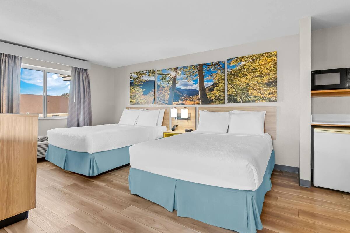 Habitación de hotel con dos camas, un escritorio, un microondas y un ventanal grande con cortinas.