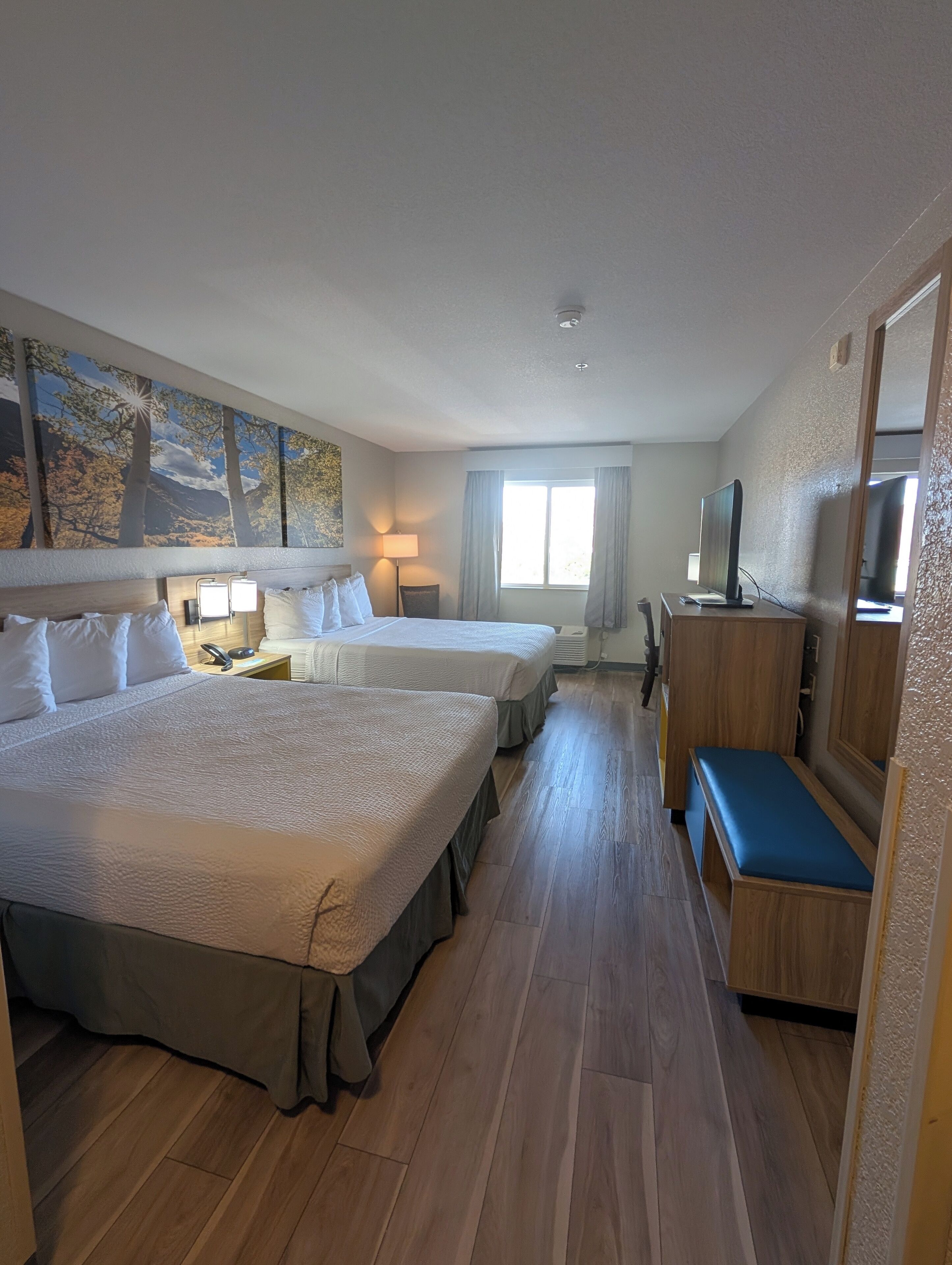 A hotel room with two beds, a desk, a chair, a TV, and a window with curtains.