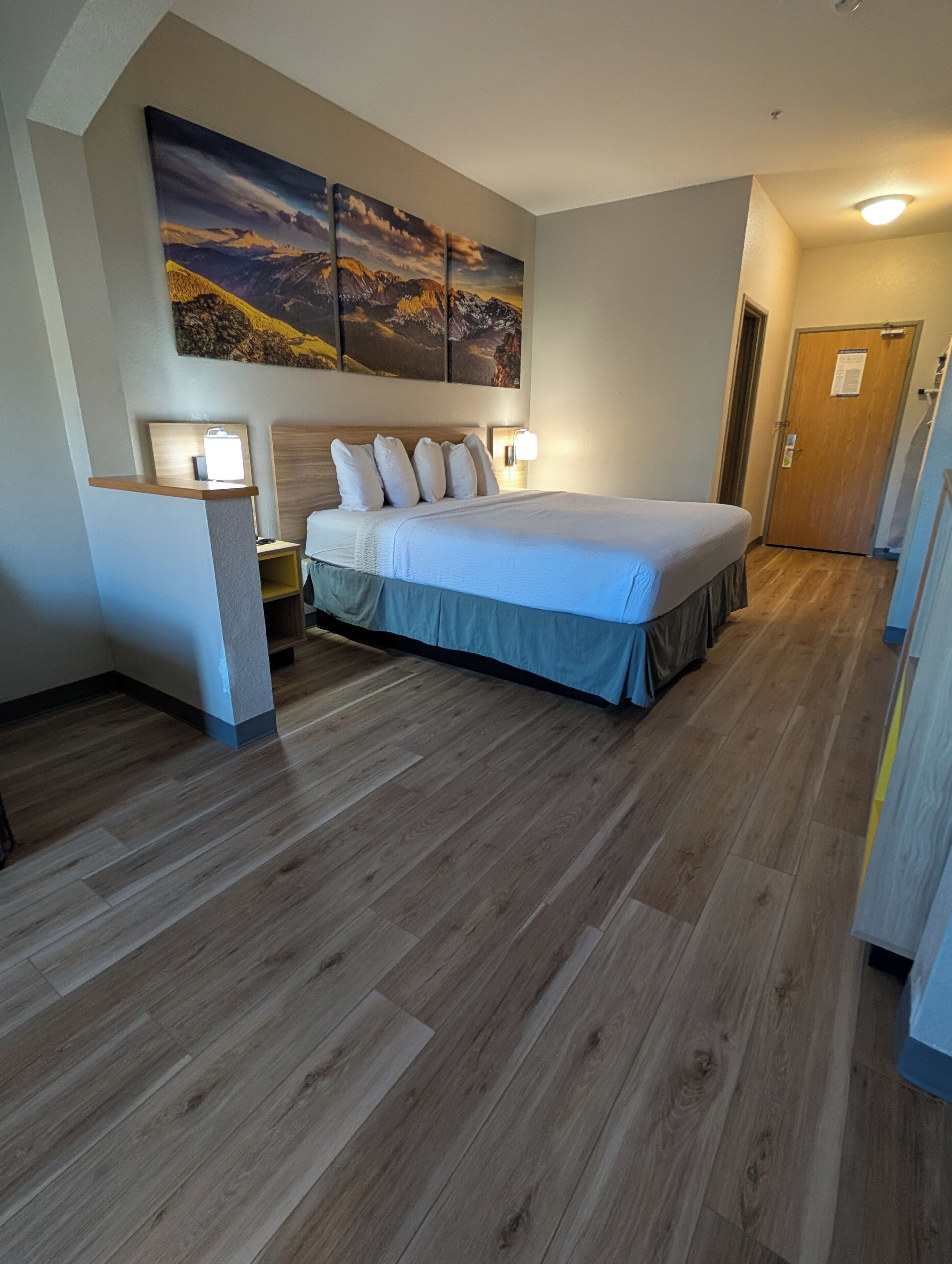 Een hotelkamer met een groot bed, houten vloeren en een schilderij aan de muur.