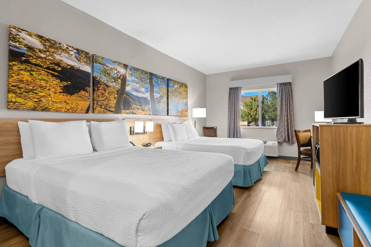 Habitación de hotel con dos camas, televisión, escritorio y un amplio ventanal con cortinas.