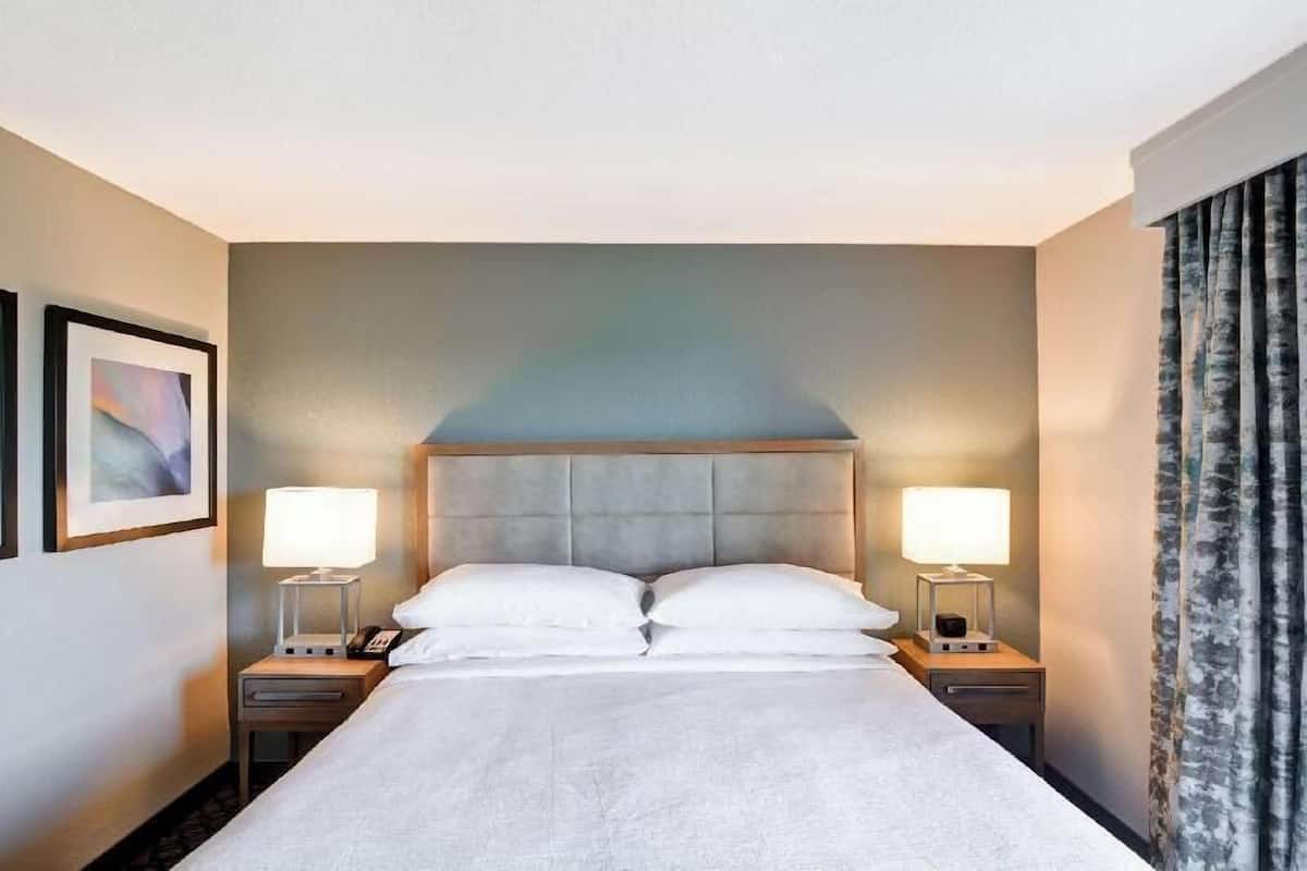 A hotel room with a large bed, two bedside tables with lamps, a headboard, and a framed picture on the wall.