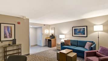Habitació d'hotel amb un sofà blau, un armari rosa, escriptori amb làmpada, petita cuina i un quadre al mur.