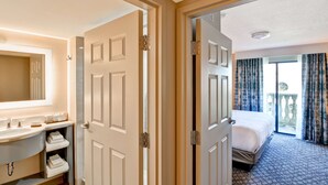 Habitación de hotel con baño, cama y balcón con cortinas.