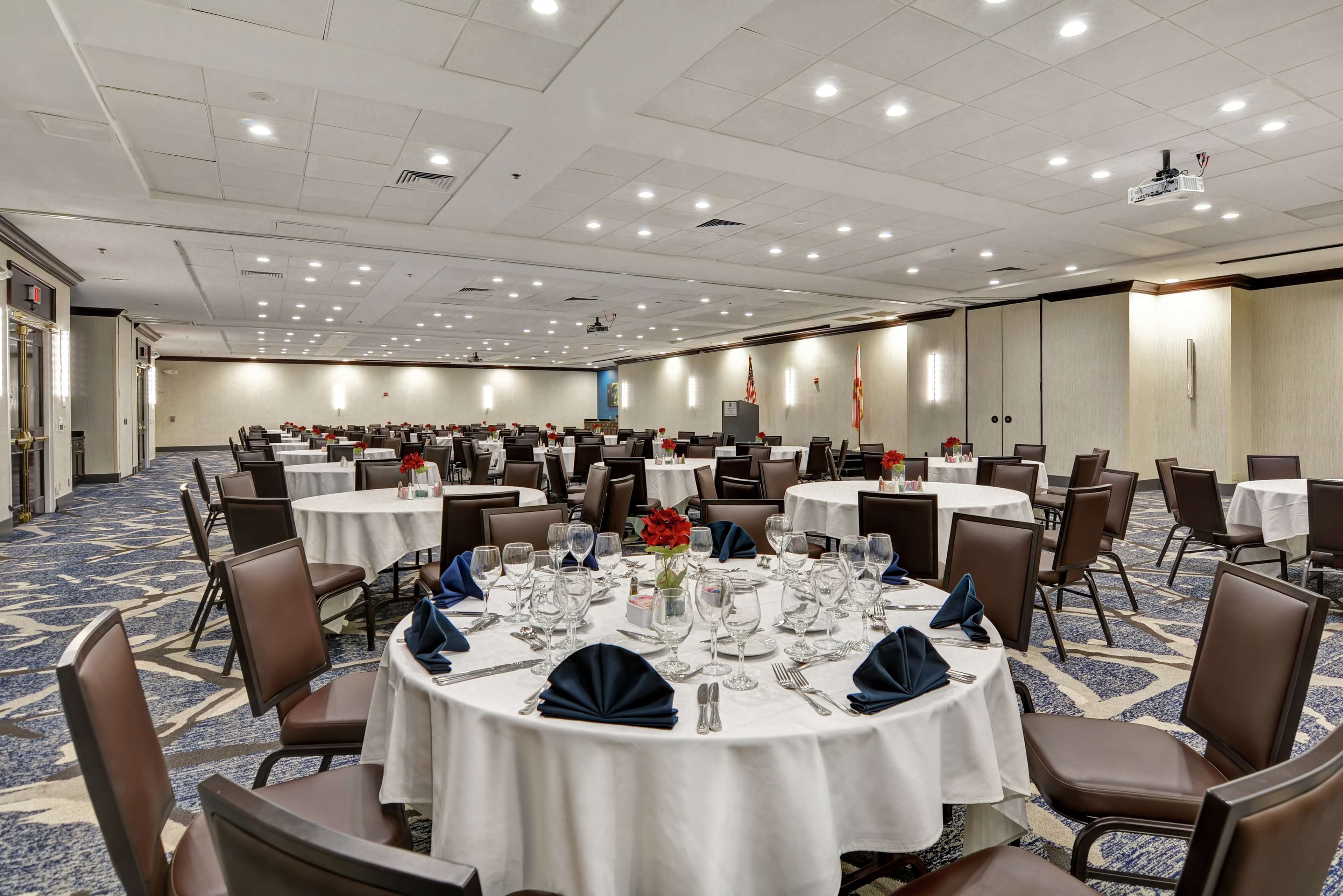 A large conference room with multiple round tables, each set with white tablecloths, chairs, and dining essentials.