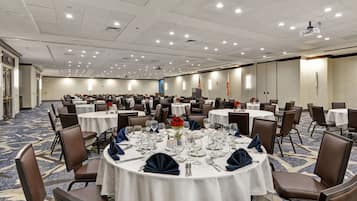 A large conference room with multiple round tables, each set with white tablecloths, chairs, and dining essentials.