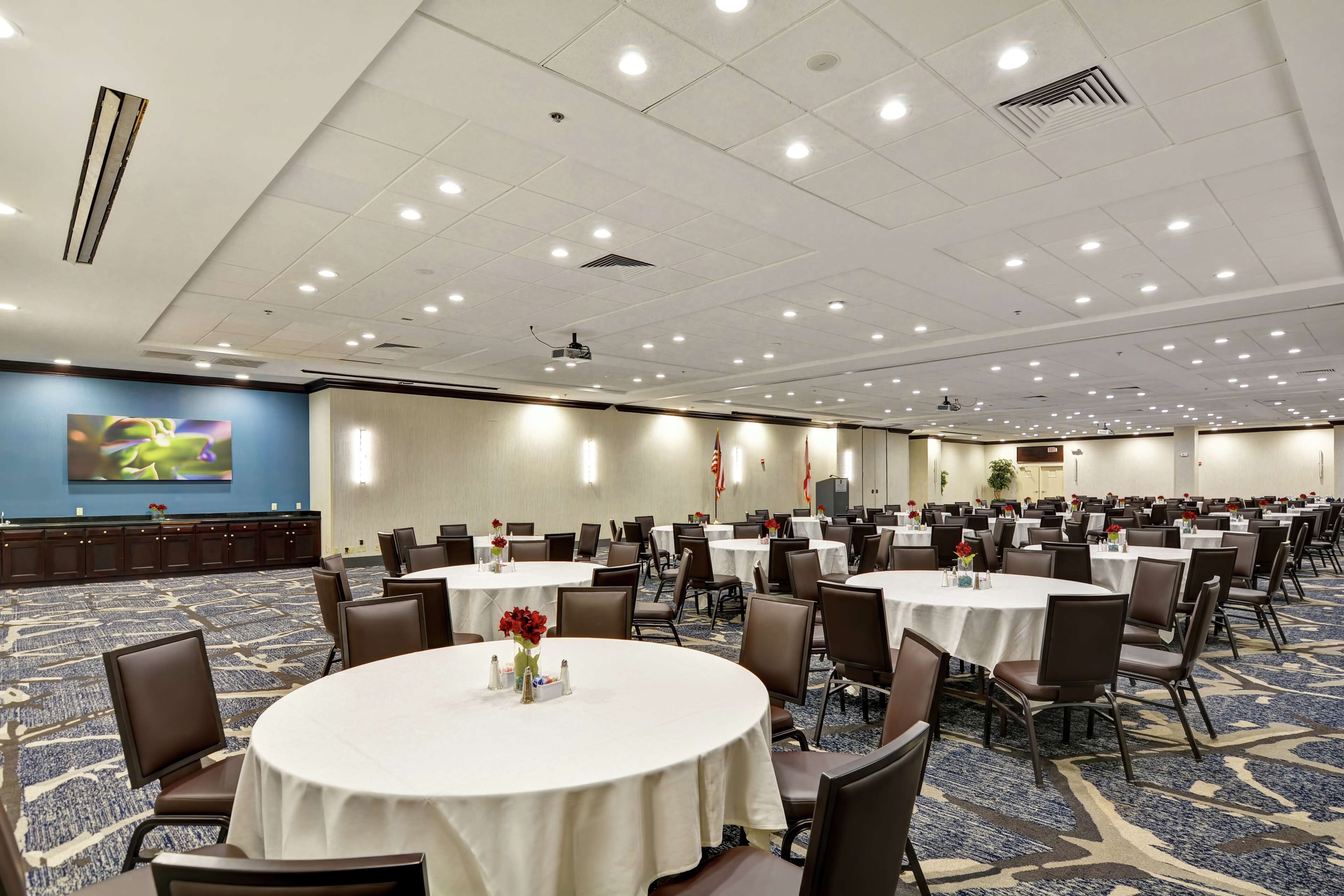A large conference room with multiple round tables, chairs, and a large screen on the wall.