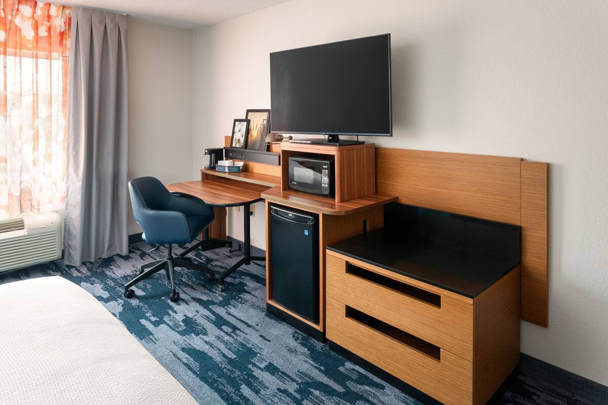 A hotel room with a bed, a desk with a computer, a television, a microwave, and a small refrigerator.
