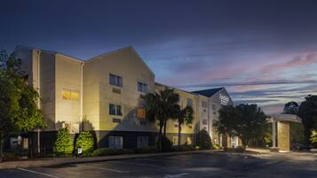 A multi-story hotel with a flat roof, large windows, and a parking lot.