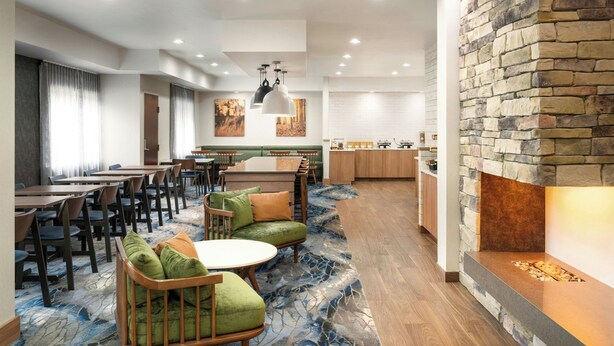 A modern hotel lobby with a dining area, seating arrangements, and a stone fireplace. - Fairfield Inn Tallahassee North/I-10 (Tallahassee)