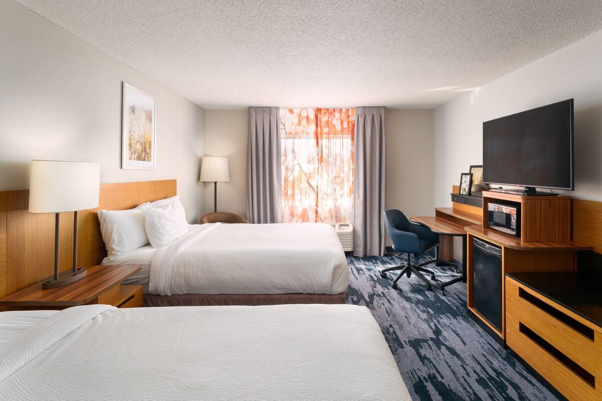 A hotel room with two beds, a desk with a television, a microwave, and a chair.