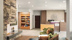 A hotel lobby with a stone wall, a reception desk, a seating area with a cushioned chair, and a snack shelf. - Fairfield Inn Tallahassee North/I-10 (Tallahassee)