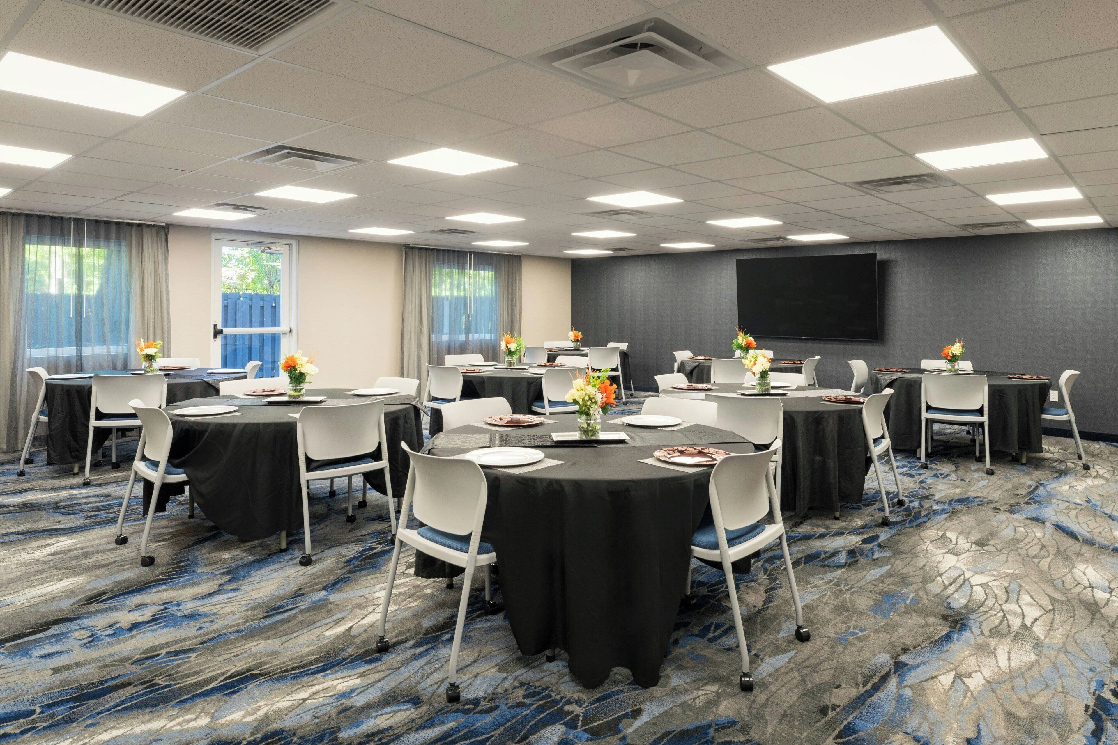 A conference room with round tables, white chairs, and black tablecloths.