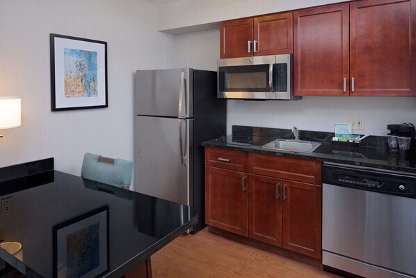 A modern kitchen with stainless steel appliances, wooden cabinets, and a black countertop. - Homewood Suites by Hilton Orlando-Maitland (Maitland)