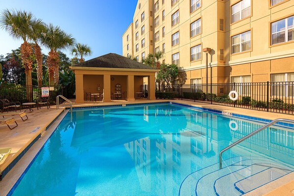 A swimming pool with lounge chairs and a covered seating area, surrounded by a fence and palm trees. - Homewood Suites by Hilton Orlando-Maitland (Maitland)