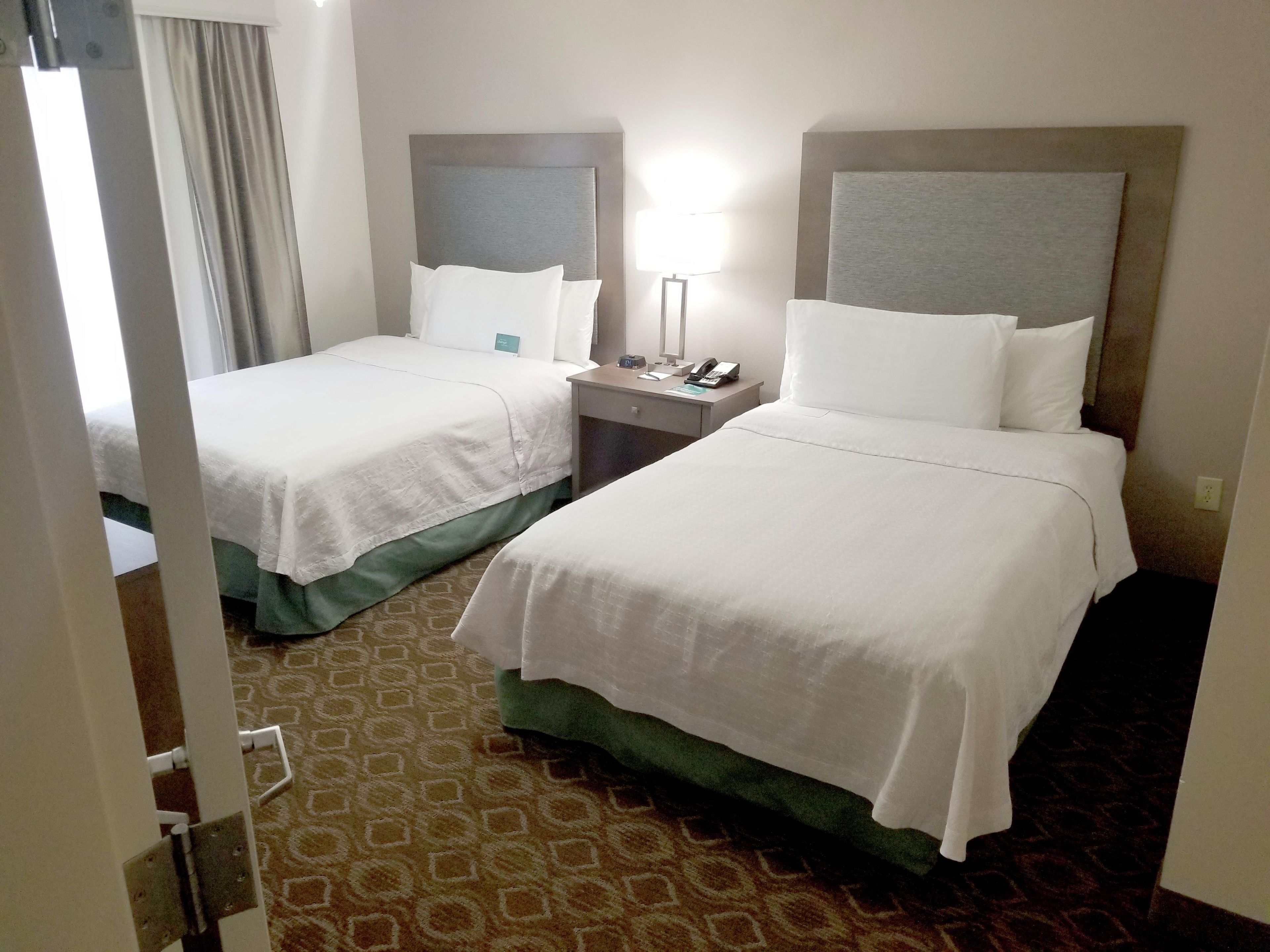 A hotel room with two beds, a nightstand, a lamp, and a patterned carpet.