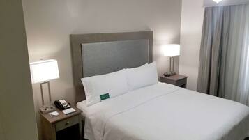 A hotel room with a neatly made bed, two bedside tables with lamps, a telephone, and a small desk with a notepad and pen.