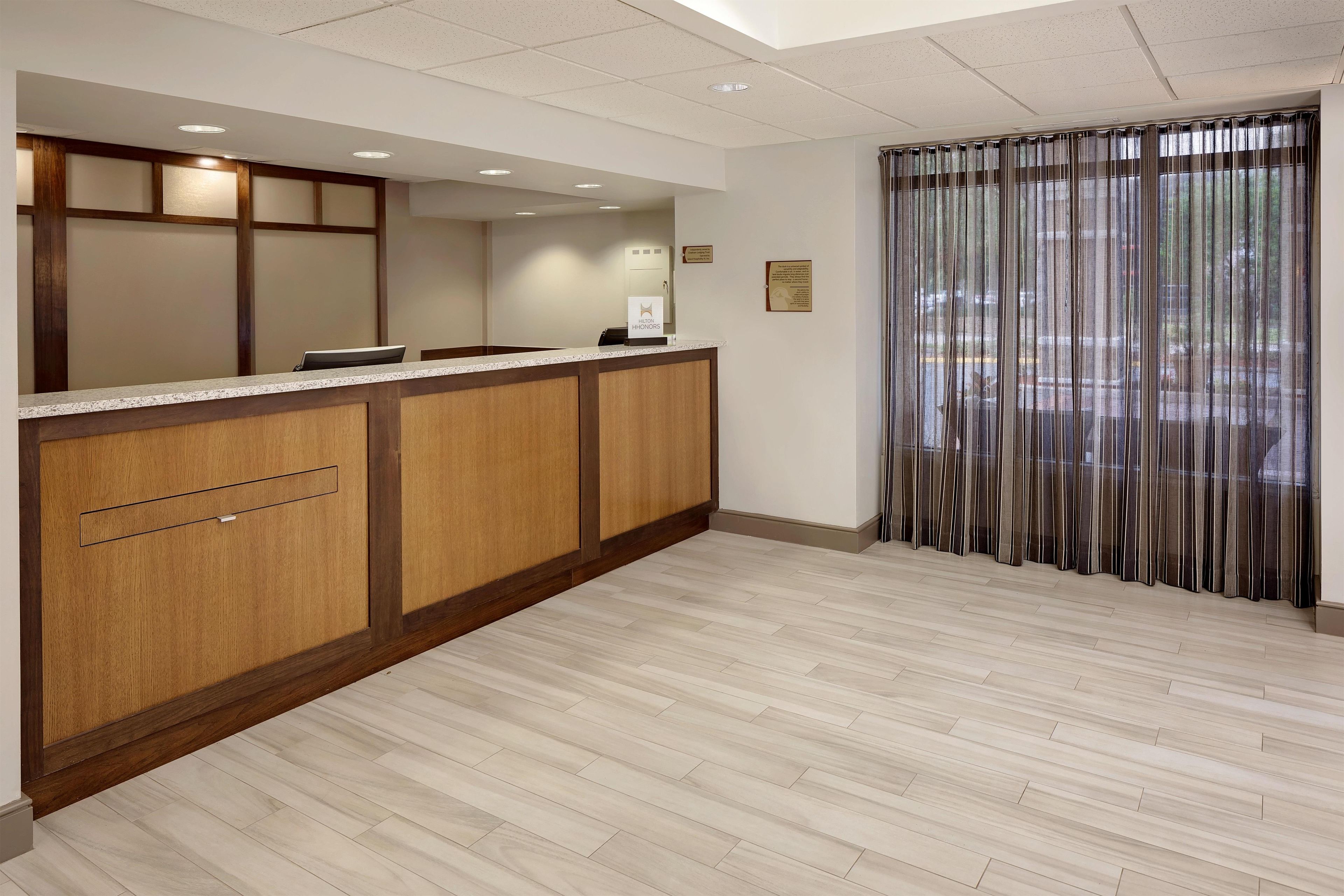 A hotel reception area with a wooden reception desk, a counter, and a large window with curtains.